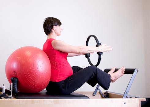 pexels photo 1103242 1103242 A pregnant woman in a red top practicing Pilates using a fitness ring and exercise ball in a gym setting.