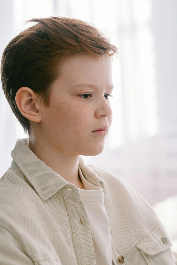 A contemplative young boy with freckles in a soft indoor setting.